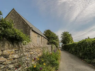 a stone wall next to a street with flowers at Herdwick Cottage in Grange Over Sands