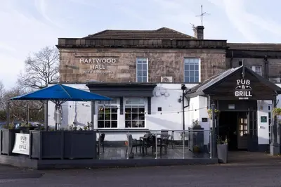 a restaurant with an umbrella in front of a building at Hartwood Hall by Greene King Inns in Chorley