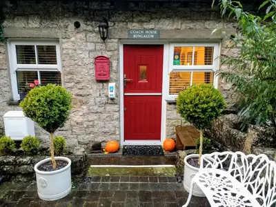a red front door of a stone house with pumpkins at Coachhousebungalow in Grange Over Sands