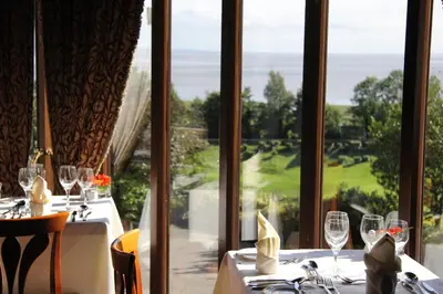 a dining room with a view of the golf course through windows at Netherwood Hotel & Spa in Grange Over Sands