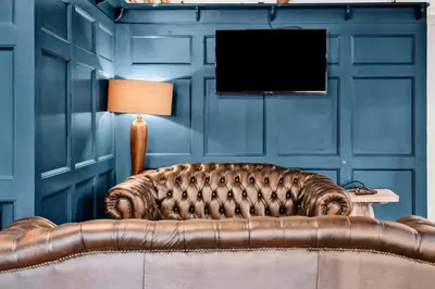 a brown leather couch in a blue room with a television at Pyes Mill Hotel Conder Green in Conder Green