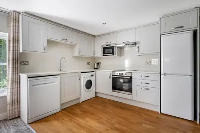 a white kitchen with white appliances and wooden floors at Thurnham Hall Resort in Cockerham