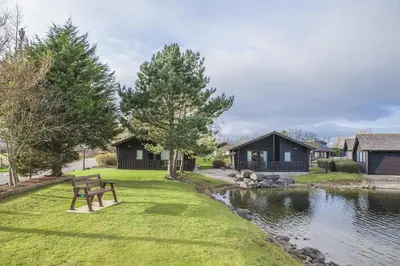 a bench sitting on the grass next to a river at Pine Lake Resort in Carnforth