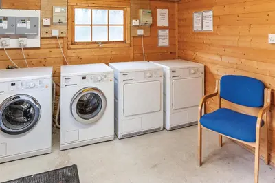 a laundry room with three washing machines and a blue chair at Pine Lake Resort in Carnforth