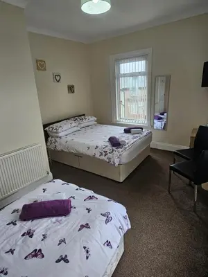a bedroom with two beds and a chair and a window at Bayswater House in Blackpool