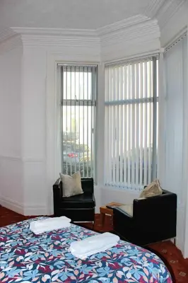 a bedroom with two chairs and a bed and windows at Belroy Hotel in Blackpool
