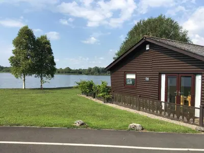 a small cabin with a lake in the background at Tegid Lodge- Pine Lake Resort in Carnforth