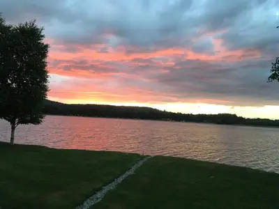 a sunset over a body of water with a tree at Tegid Lodge- Pine Lake Resort in Carnforth