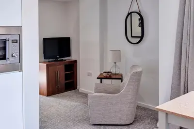 a living room with a tv and a chair and a table at Staybridge Suites Liverpool by IHG in Liverpool