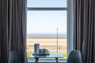 a room with a table and a window with a view of the beach at The Clifton Seafront Hotel in Morecambe