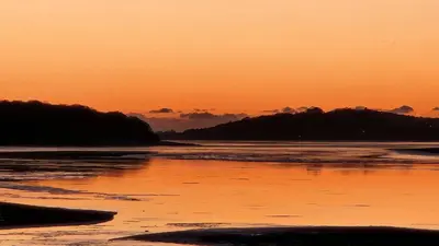 a sunset over a beach with trees in the background at Ye Olde Fighting Cocks in Arnside