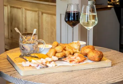 a table with a plate of food and two glasses of wine at Ye Olde Fighting Cocks in Arnside