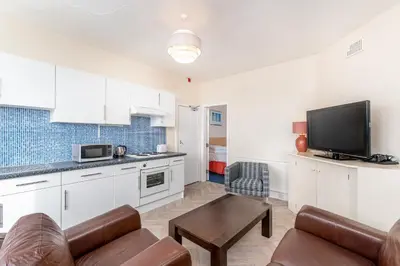 a kitchen with white cabinets and a living room at Sandpiper Holiday Apartments in Blackpool
