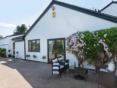 a white house with chairs and a plant with flowers at Buttercup Cottage in Halsall