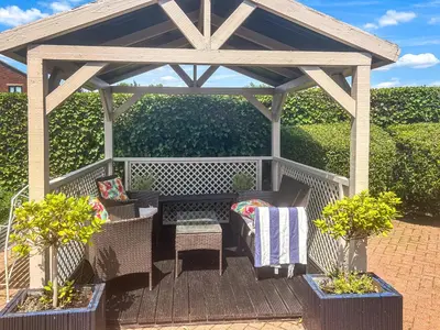 a pergola with chairs and a table on a deck at Buttercup Cottage in Halsall