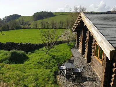a cabin with a table and chairs and a field at Newland Valley Log Cabins in Ulverston