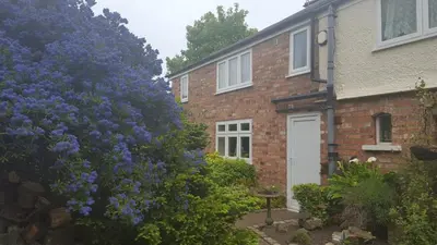a brick house with a white door and purple flowers at The Coach House Holiday Cottage, Southport in Southport