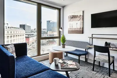 a living room with a blue couch and a large window at Citadines City Centre Liverpool in Liverpool