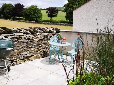 a table and chairs on a patio with a stone wall at Yew Fold in Soutergate