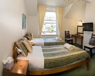 two beds in a room with a desk and a window at Somerset House B&B in Grange Over Sands