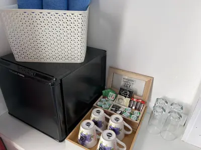 a counter with a black refrigerator and a shelf with cups at Backpackers Blackpool Hotel & Suites in Blackpool