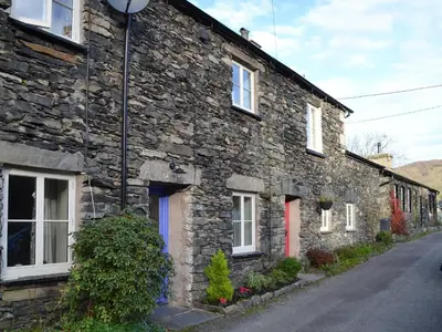 a stone house with a red door on a street at Coopers Cottage in Haverthwaite