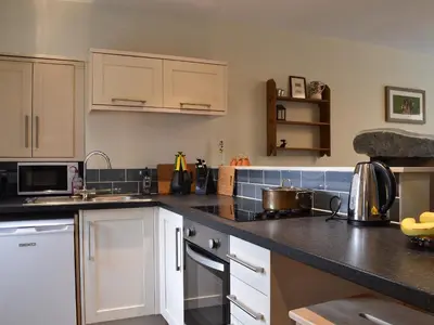 a kitchen with white cabinets and black counter tops at Coopers Cottage in Haverthwaite
