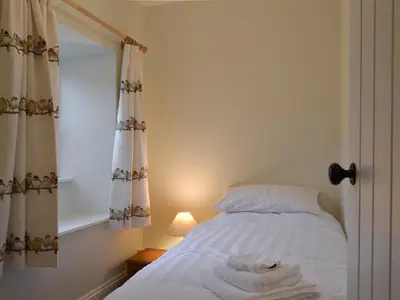 a bedroom with a bed with white sheets and a window at Coopers Cottage in Haverthwaite