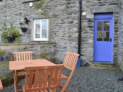 a table and chairs in front of a stone building with a blue door at Coopers Cottage in Haverthwaite