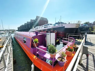 a boat docked at a dock with potted plants on it at The Joker Boat in Liverpool