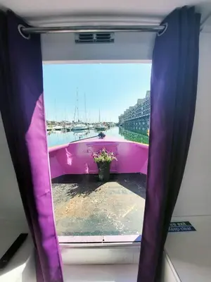 a window with a purple curtain and a vase of flowers at The Joker Boat in Liverpool