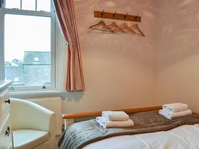 a bedroom with a bed and a chair and a window at Lythdene in Grange Over Sands