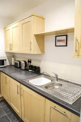 a kitchen with a sink and wooden cabinets at Ropewalks Apartments by Happy Days in Liverpool