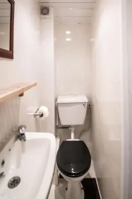 a white bathroom with a black toilet and a bath tub at MyRoomz Hollingdales Hotel in Blackpool