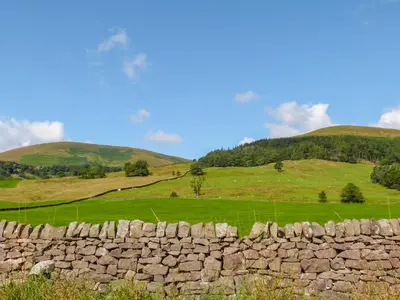 a stone wall in a field with hills in the background at 3 Poole End in Clitheroe