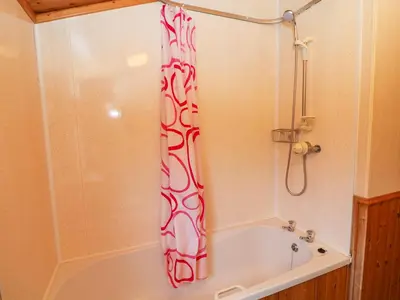 a bath tub with a red and white shower curtain at The Cedars in Carnforth