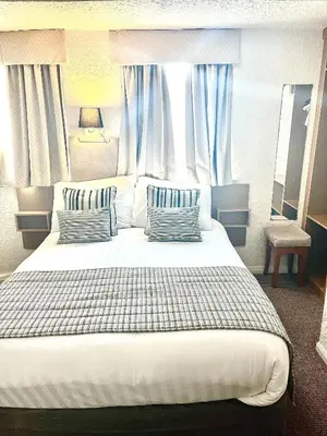 a bedroom with a large white bed with blue curtains at Clifton Court Hotel in Blackpool