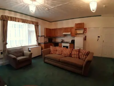 a living room with a couch and chairs and a kitchen at Rosemede Holiday Flats in Blackpool