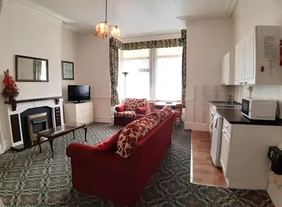 a living room with a red couch and a kitchen at Rosemede Holiday Flats in Blackpool