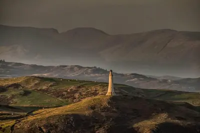 a lighthouse on a hill with mountains in the background at Tethera at Coal Yeat in Spark Bridge