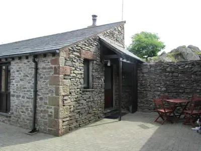 a stone building with a table and chairs in front of it at Tethera at Coal Yeat in Spark Bridge