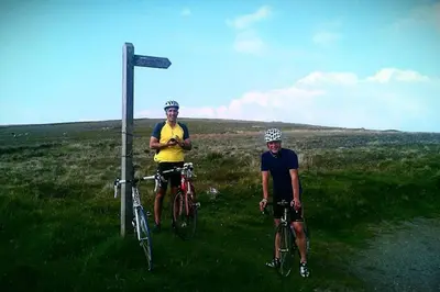 two men are standing next to their bikes in a field at Tethera at Coal Yeat in Spark Bridge