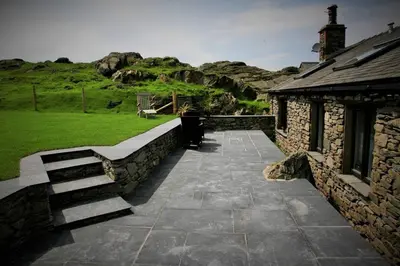 a stone building with a bench and a stone wall at Tethera at Coal Yeat in Spark Bridge