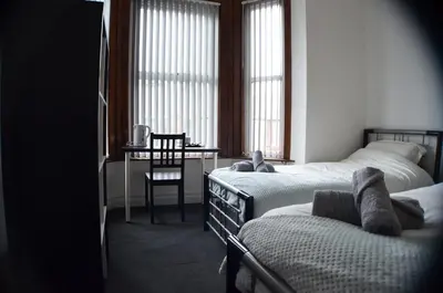 a bedroom with two beds and a desk and windows at Old Swan Guest House in Liverpool
