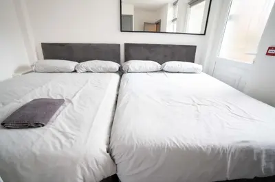 two beds with white sheets and a mirror on the wall at Urban Apartment Free Parking Near Pleasure Beach in Blackpool