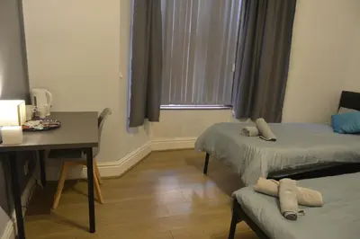 a room with two beds and a table and a desk at Kensington Guest House Liverpool in Liverpool