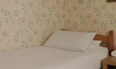 a bedroom with a bed with white sheets and floral wallpaper at Leofric Legends in Blackpool