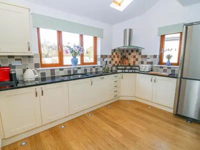 a kitchen with white cabinets and wooden floors and windows at Langtree in Carnforth