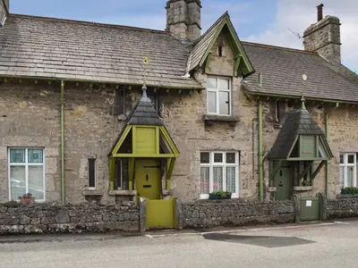 an old stone building with a yellow door and windows at Underhill Cottage in Arnside