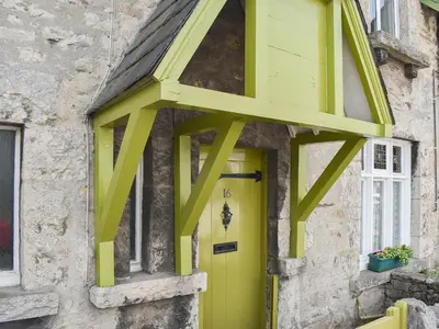 a yellow door on the side of a stone building at Underhill Cottage in Arnside